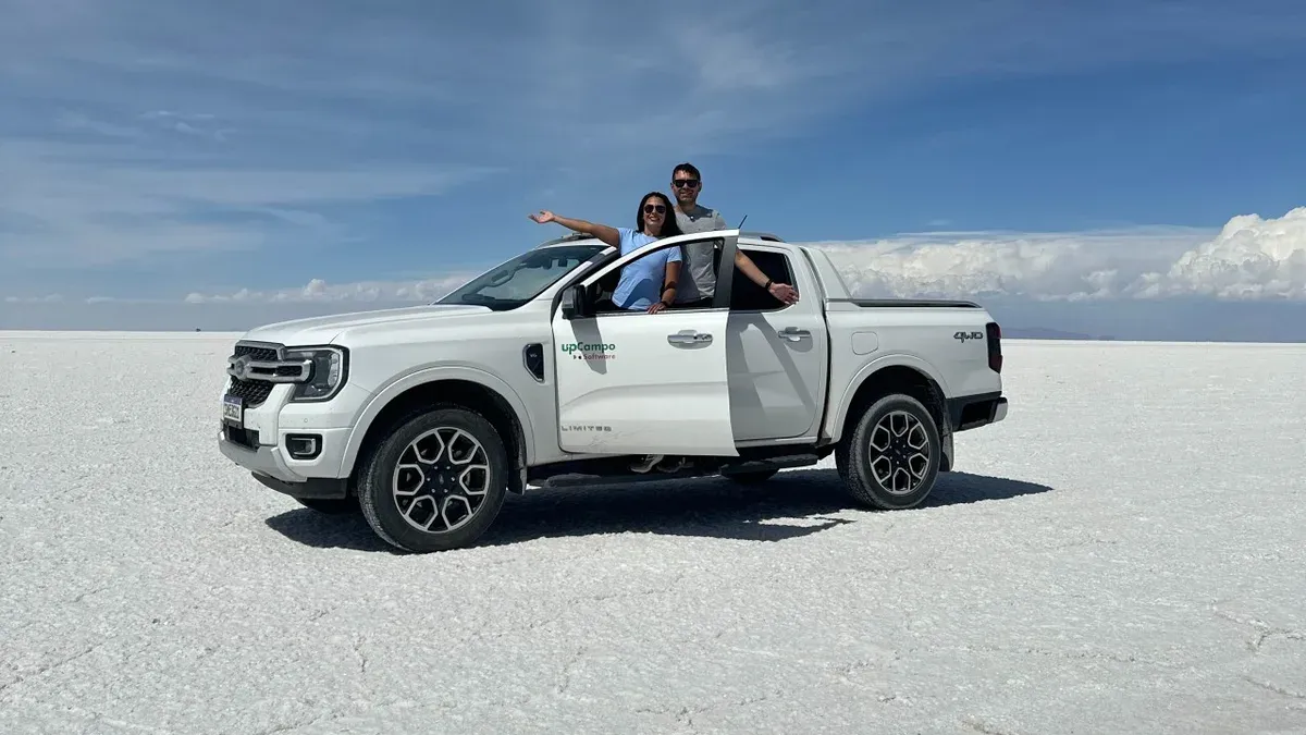 Pareja saluda desde una camioneta blanca en el Salar de Uyuni, bajo un cielo azul