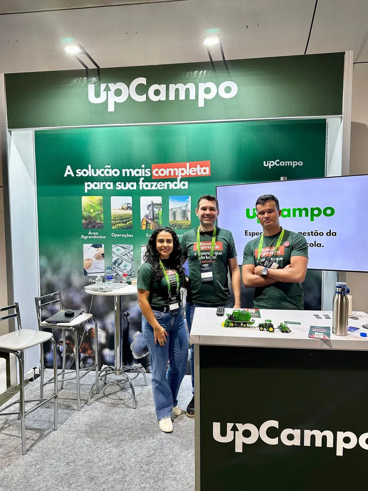 Tres personas sonrientes en el stand de upCampo en el AGRO Summit